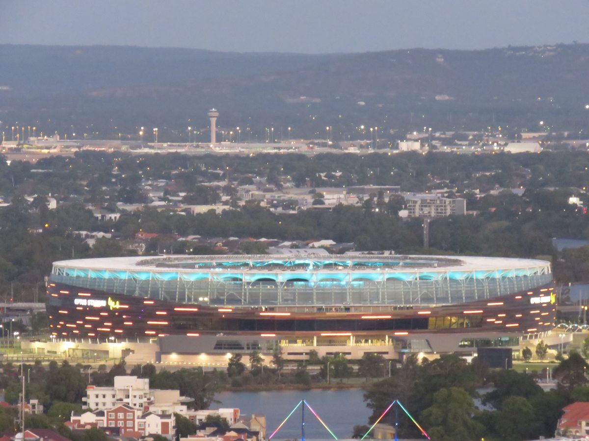Illuminated exterior of Perth Stadium seen across East Perth at dusk